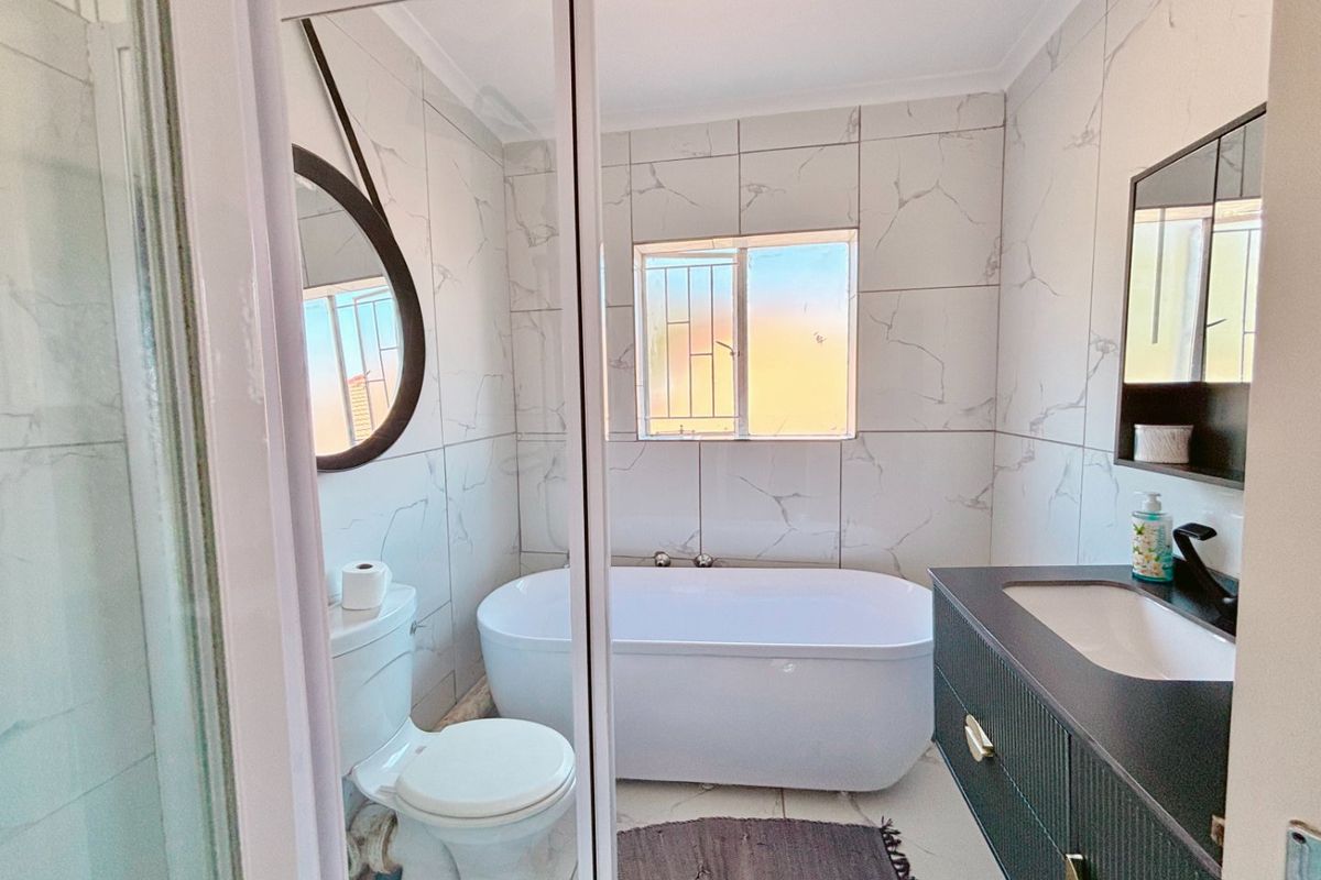 Modern bathroom featuring a freestanding bathtub, vanity cabinet with integrated sink, toilet, and a separate shower enclosure with marble-look wall tiles.