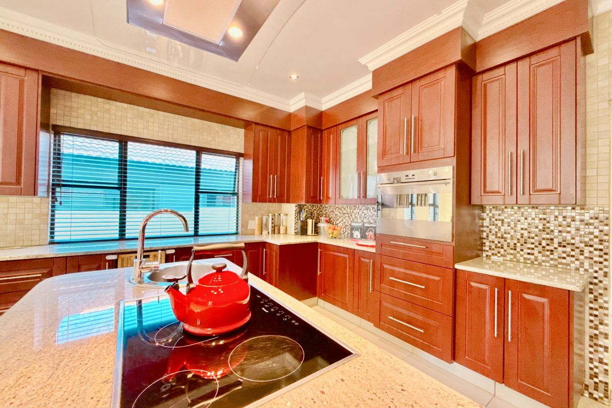 A well-appointed kitchen featuring rich wood cabinetry, granite countertops, a central island with an integrated electric hob, and a decorative mosaic tile backsplash.