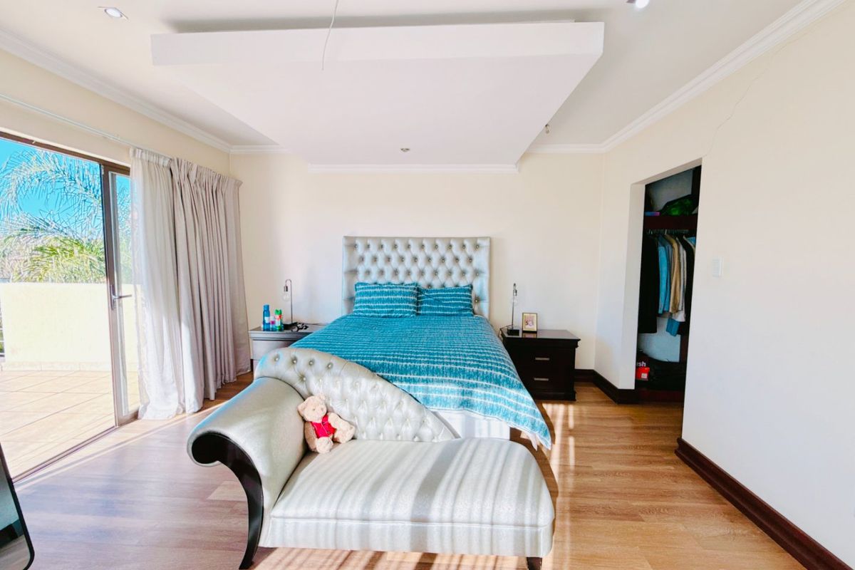 Spacious bedroom featuring laminate flooring, a recessed ceiling with downlights, a walk-in closet, and a sliding glass door leading to an outdoor balcony.