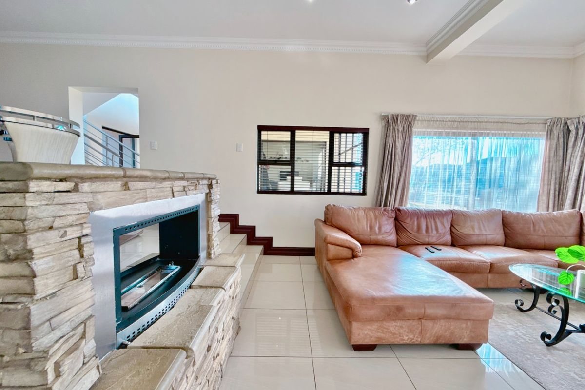 Spacious living room featuring a prominent stone-clad fireplace, polished tiled flooring, and recessed lighting, creating a bright and inviting atmosphere.
