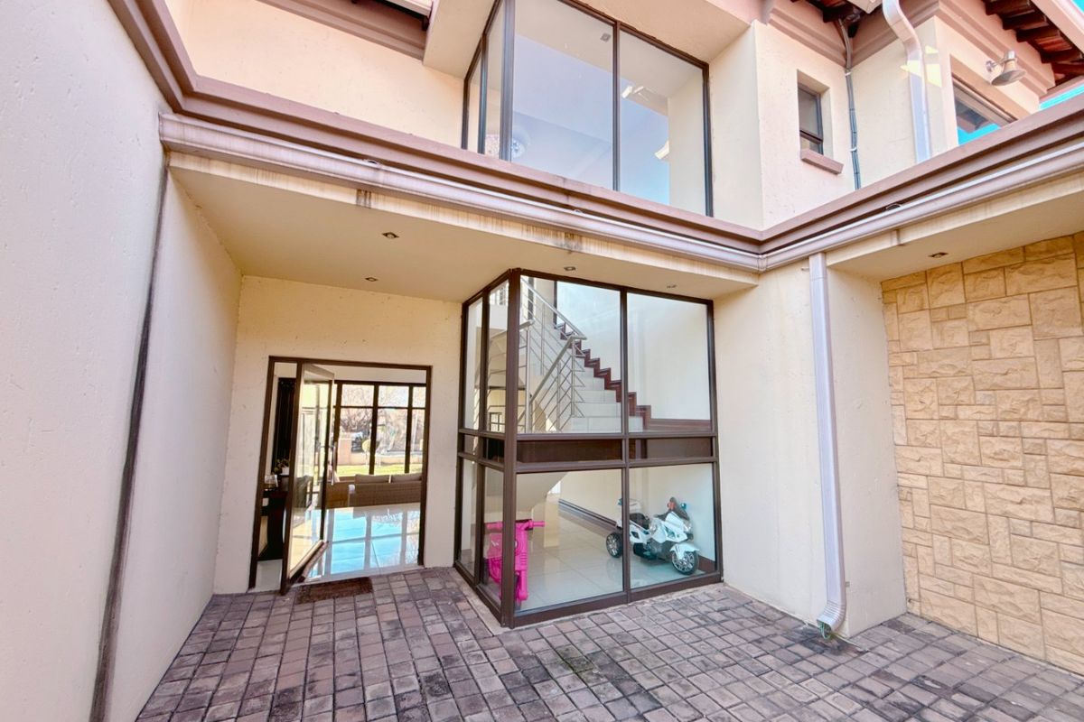 Rear courtyard featuring paved flooring, stone cladding accents, and a prominent glass-enclosed staircase area providing natural light to the interior.