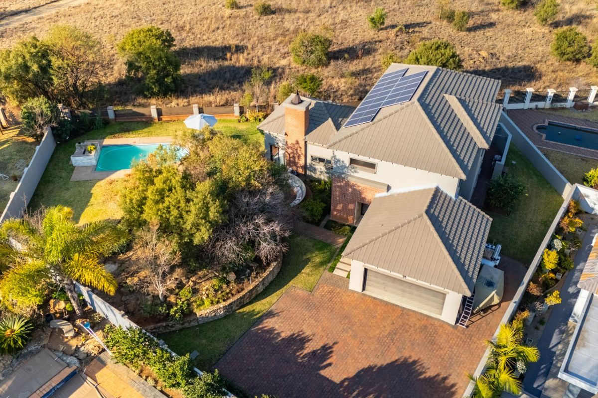 Aerial view of a residential property featuring a tiled roof with solar panels, a swimming pool, a brick driveway, and a garage.