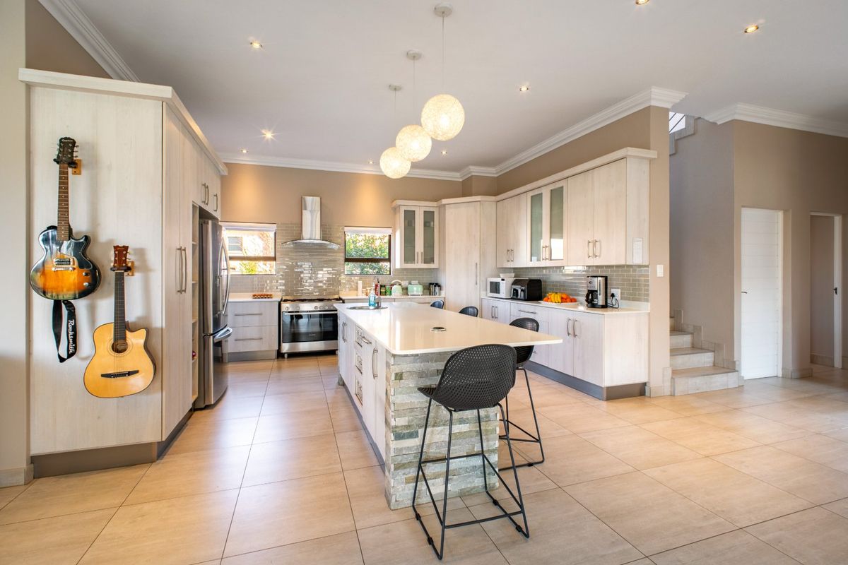 Modern kitchen featuring a central island with stone cladding, quartz countertops, stainless steel appliances, tiled backsplash, and ample built-in cabinetry.