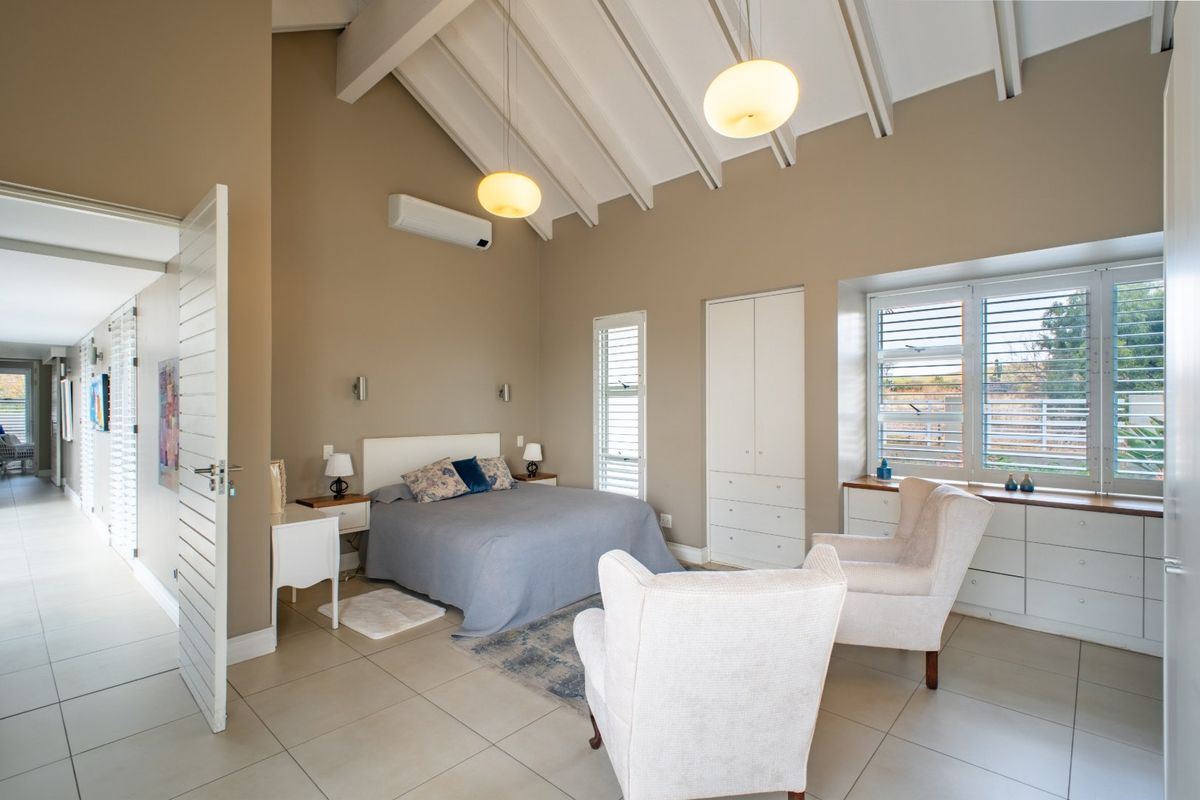 Spacious bedroom featuring a vaulted ceiling with exposed beams, built-in cabinetry, tiled flooring, and large windows with louvre shutters.
