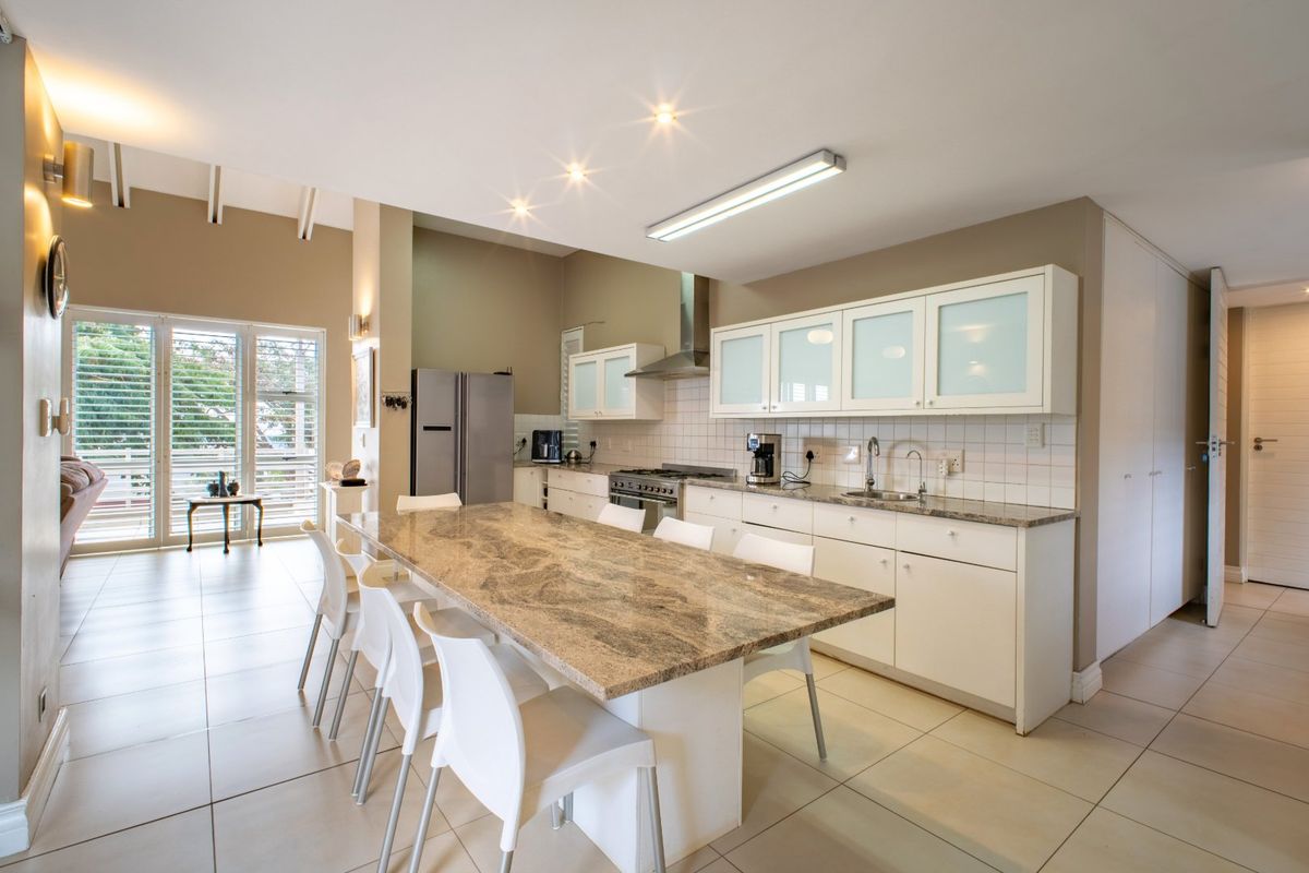 Spacious kitchen featuring a large granite island, ample built-in cabinetry, stainless steel extractor fan, and tiled flooring, seamlessly integrated into an open-plan living area.
