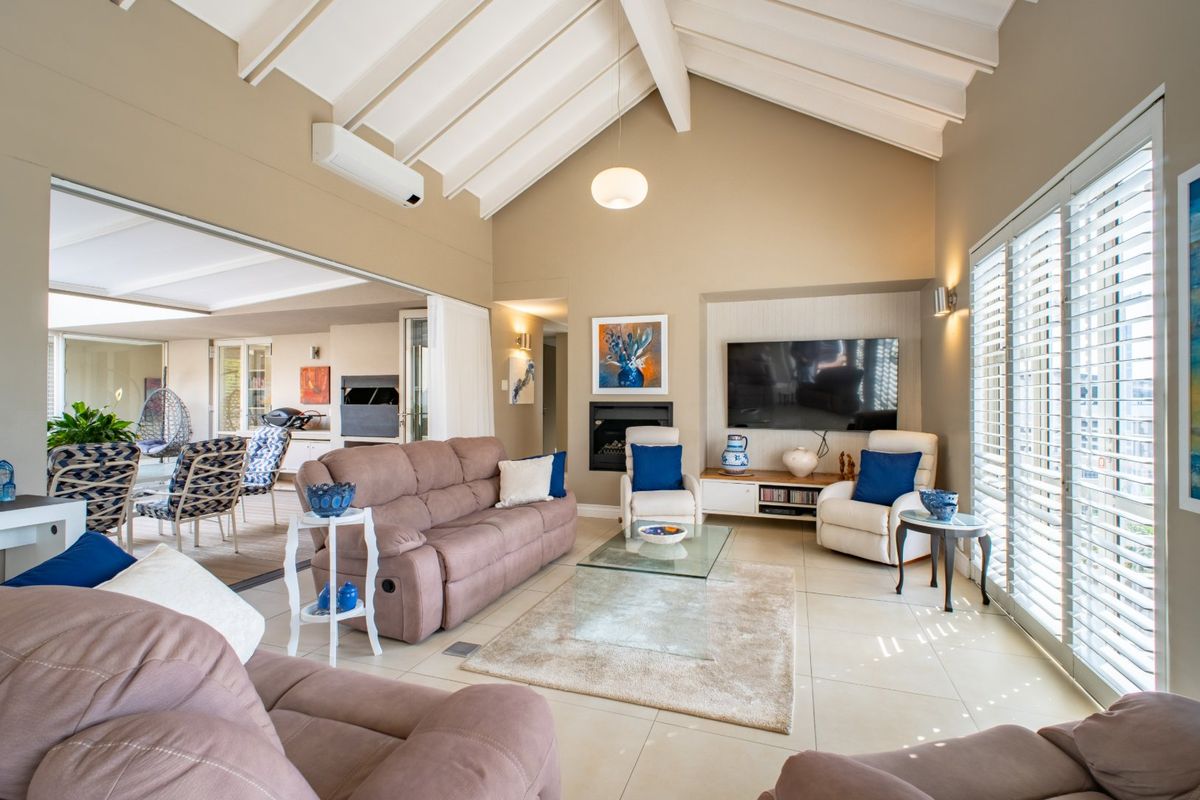 Spacious living room featuring a vaulted ceiling with exposed beams, tiled flooring, a built-in fireplace, and large sliding doors with plantation shutters.