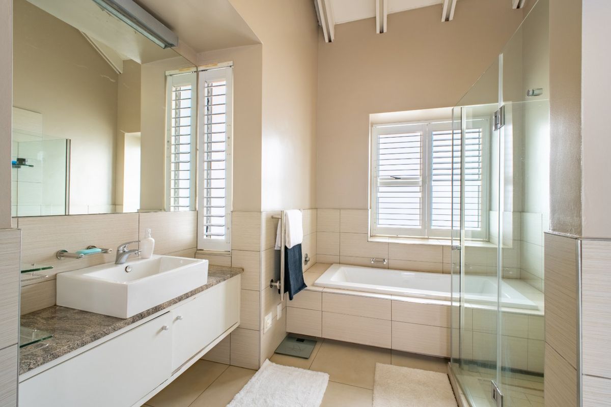 A well-maintained bathroom featuring a modern vessel sink, built-in bathtub, glass-enclosed shower, and neutral tiled finishes with shutter blinds for privacy.