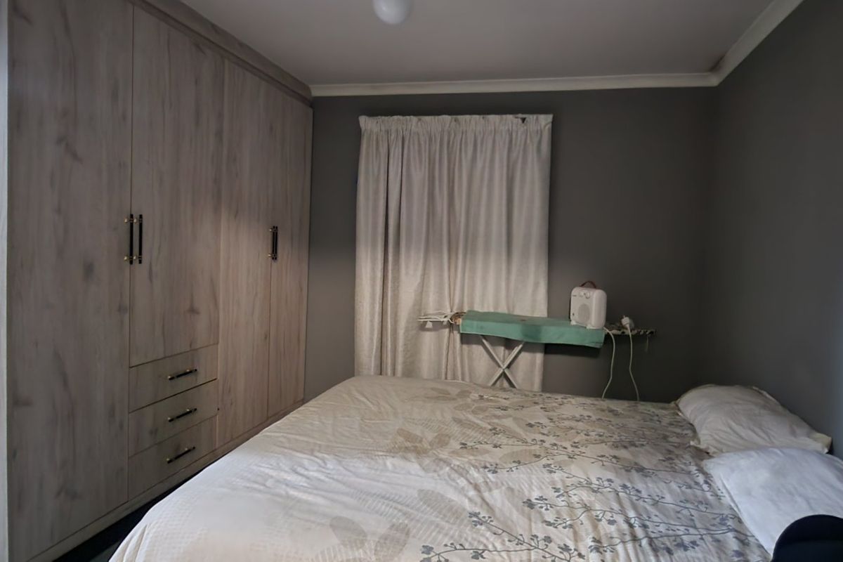 A bedroom featuring neutral grey walls and extensive light wood-grain built-in cupboards providing ample storage space.