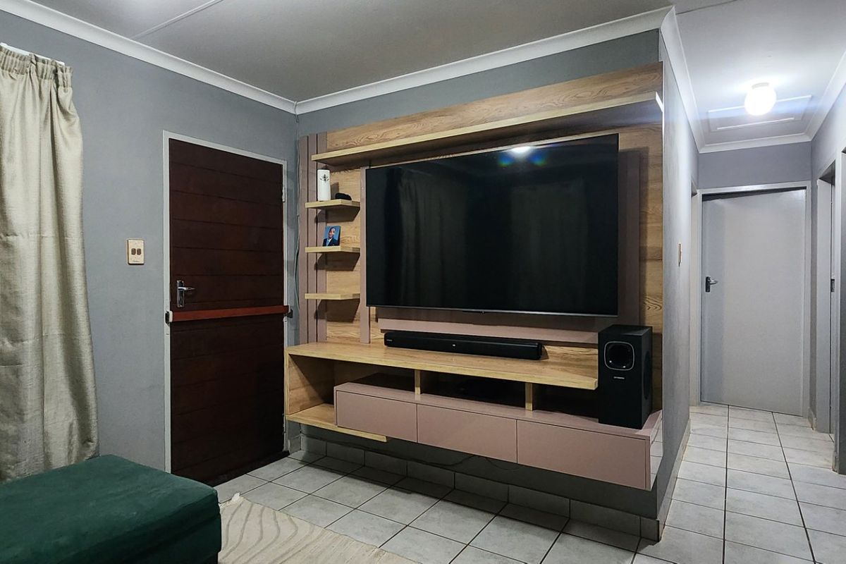 A living room featuring a modern built-in media unit, tiled flooring, and neutral wall finishes, providing a functional and well-maintained space.
