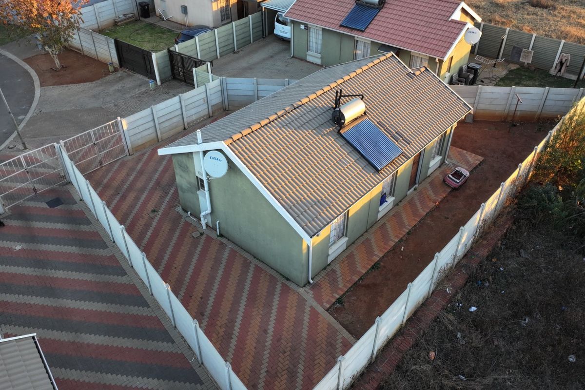 Aerial view of a residential property featuring a tiled roof with a solar water heater, paved driveway, and secure precast boundary walling.