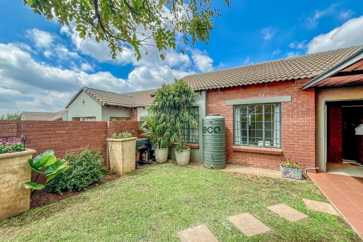 A private rear garden area featuring a brick facade, tiled roof, paved pathway, and a rainwater collection tank.