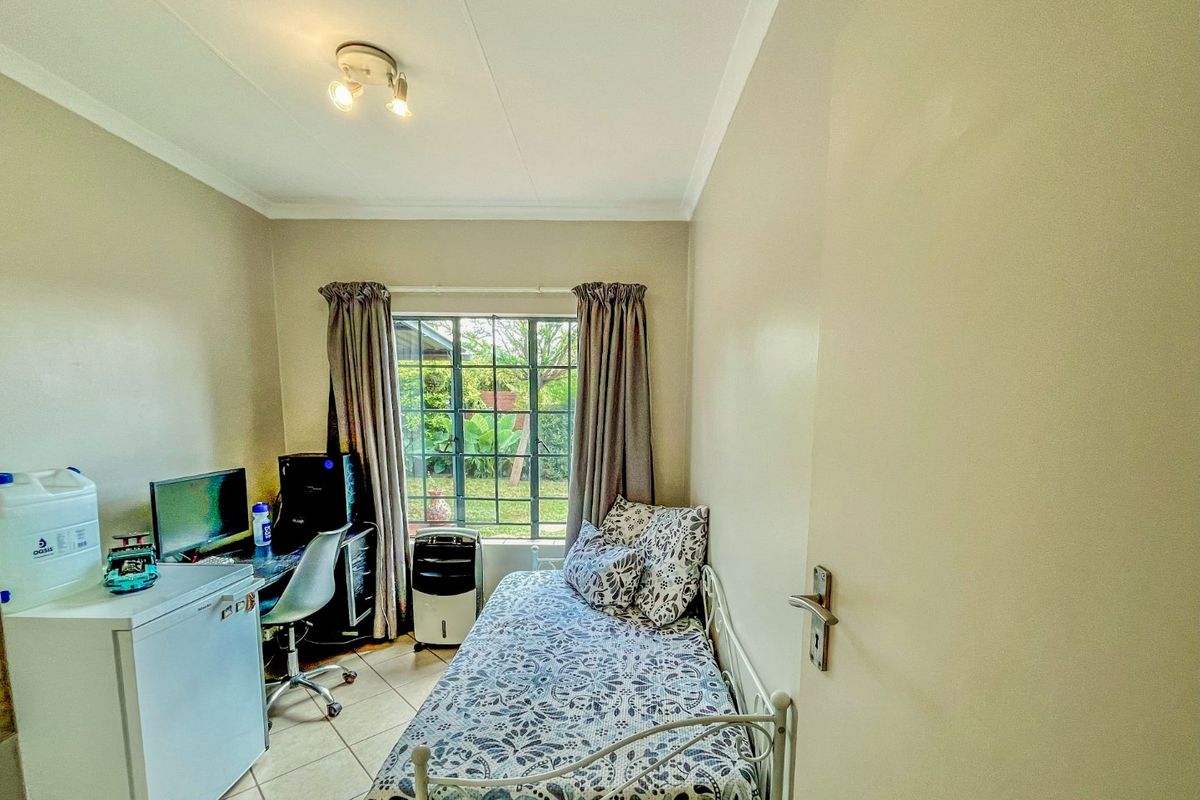 A compact bedroom featuring tiled flooring, a window with security bars, and neutral wall finishes, suitable as a guest room or home office.