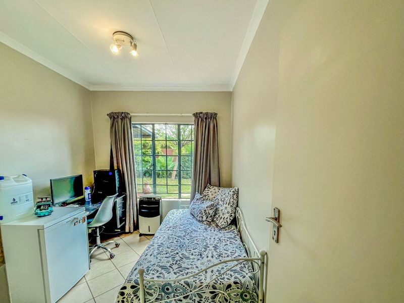 A compact bedroom featuring tiled flooring, a window with security bars, and neutral wall finishes, suitable as a guest room or home office.