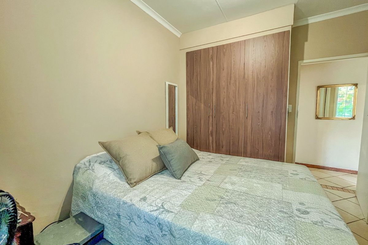 A functional bedroom featuring built-in wooden wardrobes, neutral wall finishes, and tiled flooring, providing a clean and practical living space.