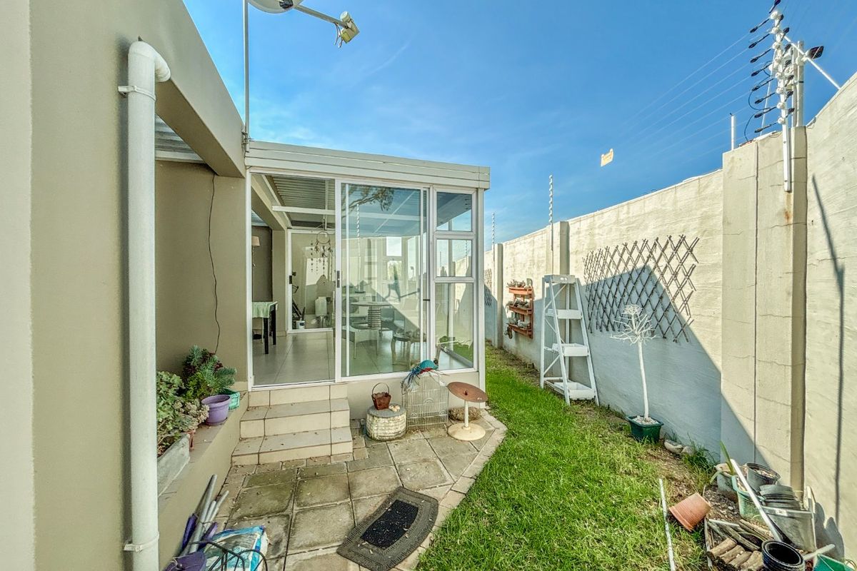 Rear garden area featuring a paved patio, enclosed sunroom with sliding glass doors, and perimeter wall with electric fencing.