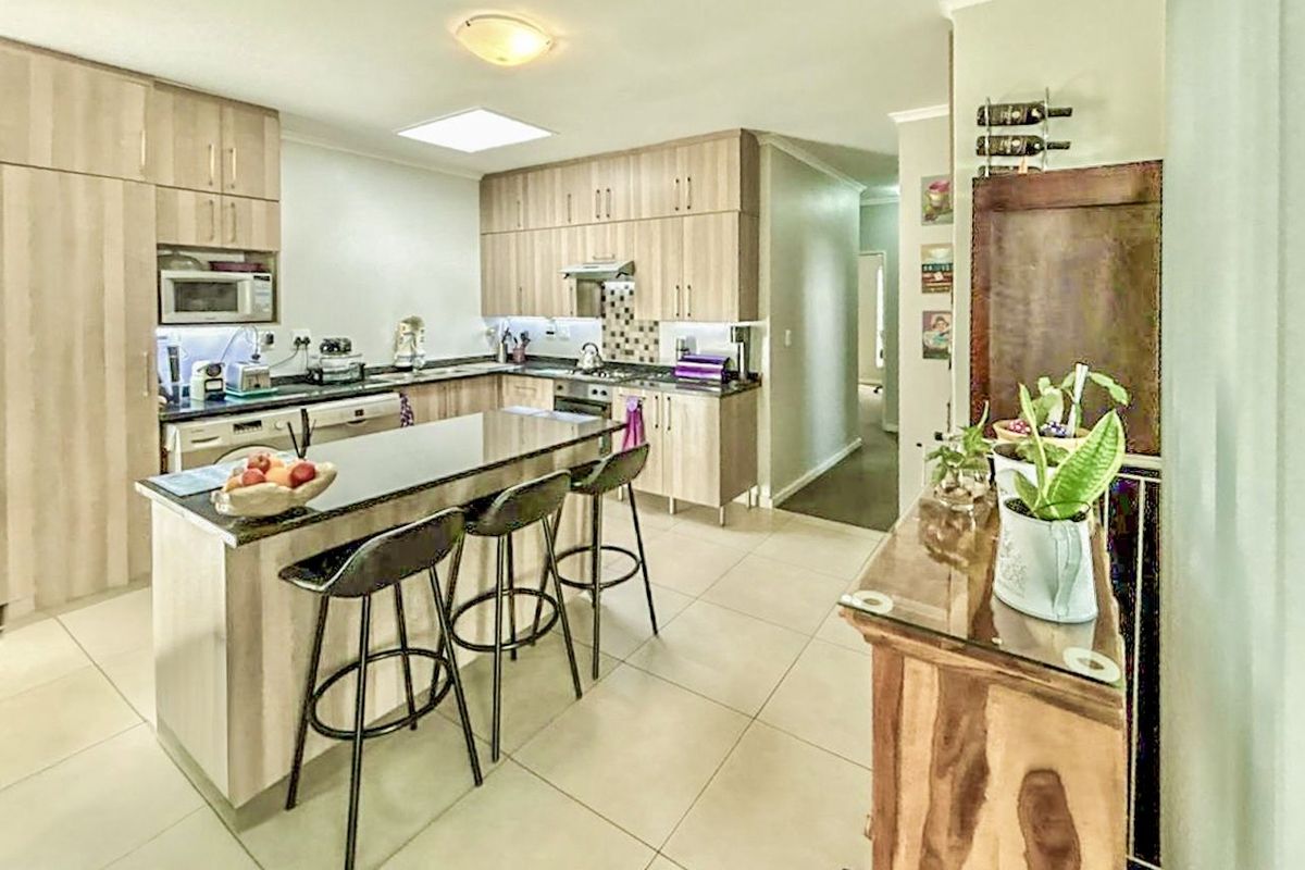 Modern kitchen featuring light wood cabinetry, granite countertops, a central island with breakfast bar seating, and integrated appliances.