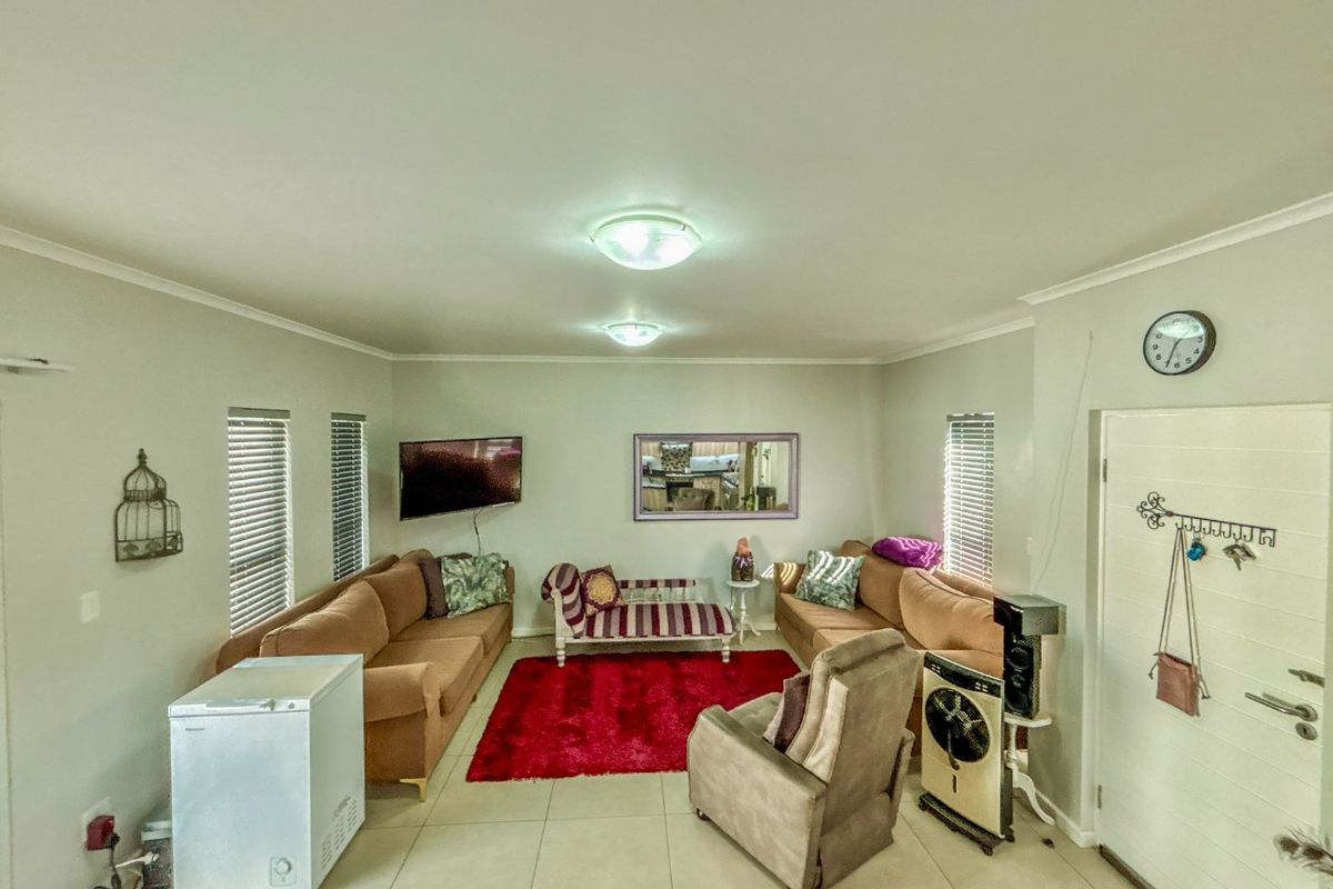 A spacious living room featuring neutral tiled flooring, flush mount ceiling lighting, and venetian blinds on the windows.