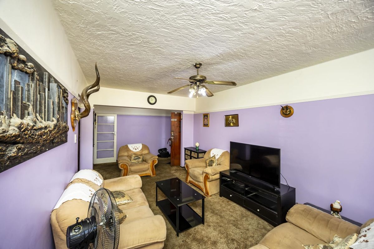 A living room featuring a ceiling fan, textured ceiling, and carpet flooring, offering a dated interior space ready for modernization.