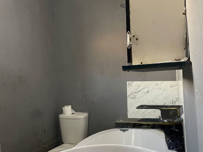 A compact bathroom featuring a basin, toilet, and medicine cabinet, currently requiring significant cosmetic updates and repairs to the ceiling and wall finishes.