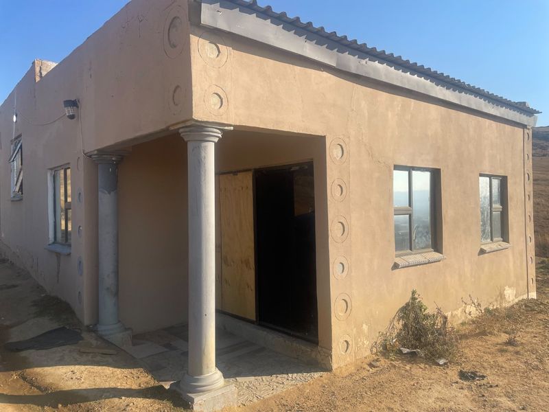 Front elevation of a single-story house featuring plastered walls, decorative columns, and aluminium window frames, requiring exterior maintenance and finishing.