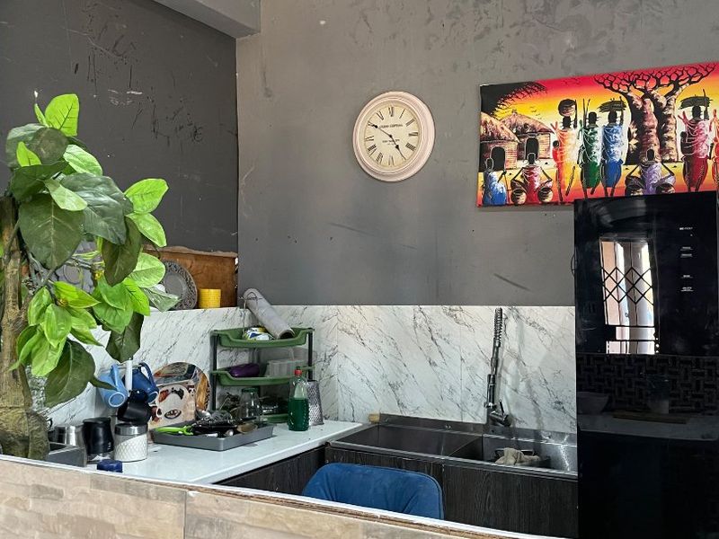A compact kitchen area featuring a double bowl sink, marble-look splashback, and stone-clad breakfast bar, currently requiring cosmetic updates to walls and ceiling.