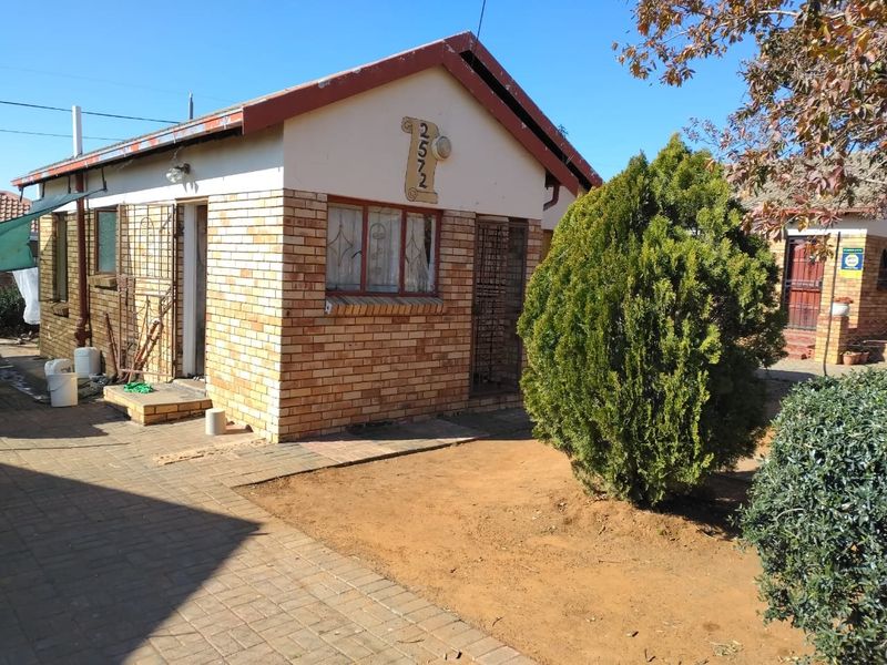 A single-story face brick house featuring a paved front area and security gate, showing signs of age and requiring exterior maintenance.