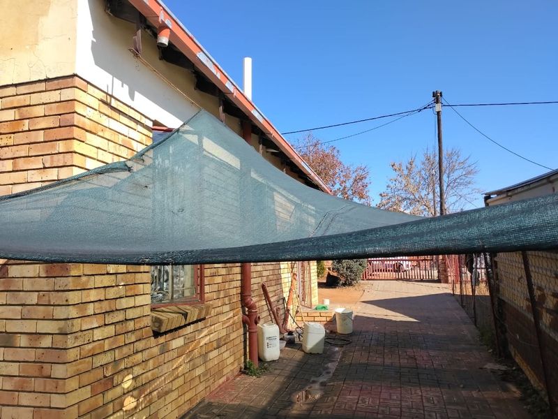 Rear exterior view of the property featuring a face brick facade, paved walkway, and installed shade cloth covering the side passage area.