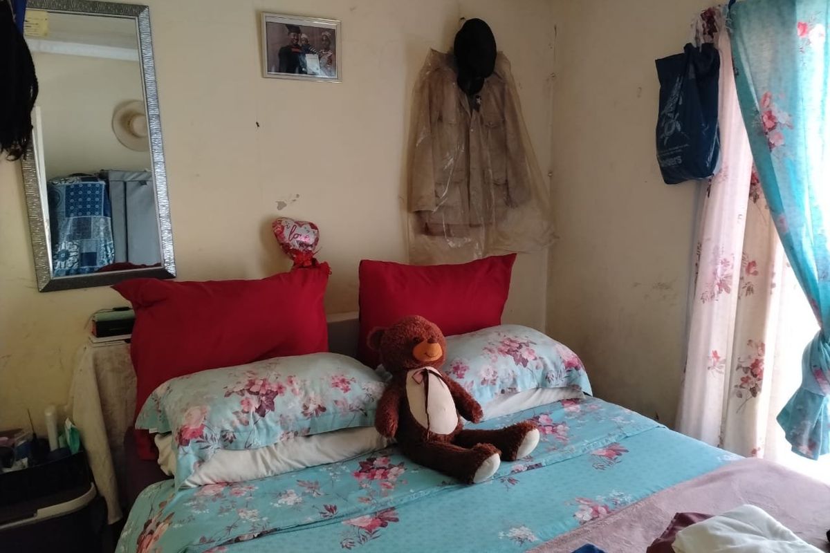 A bedroom featuring standard wall finishes and a window with curtains, showing signs of wear and surface damage on the walls.