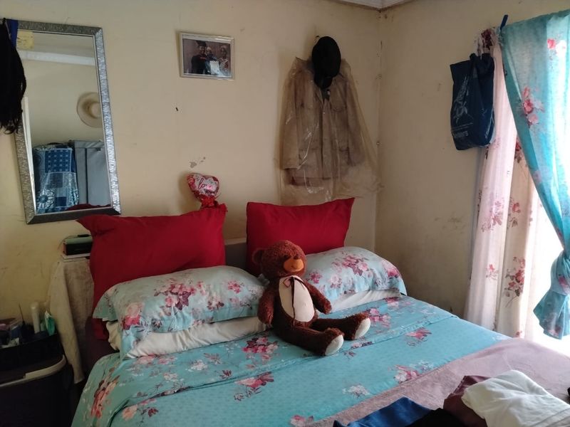 A bedroom featuring standard wall finishes and a window with curtains, showing signs of wear and surface damage on the walls.