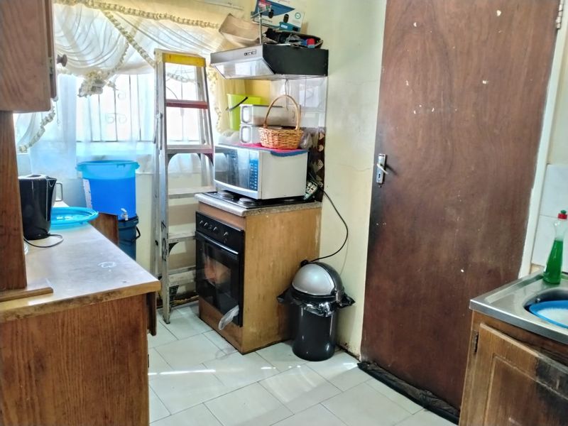 A compact kitchen featuring wooden cabinetry, a built-in oven with extractor fan, and tiled flooring, currently showing signs of wear and dated finishes.