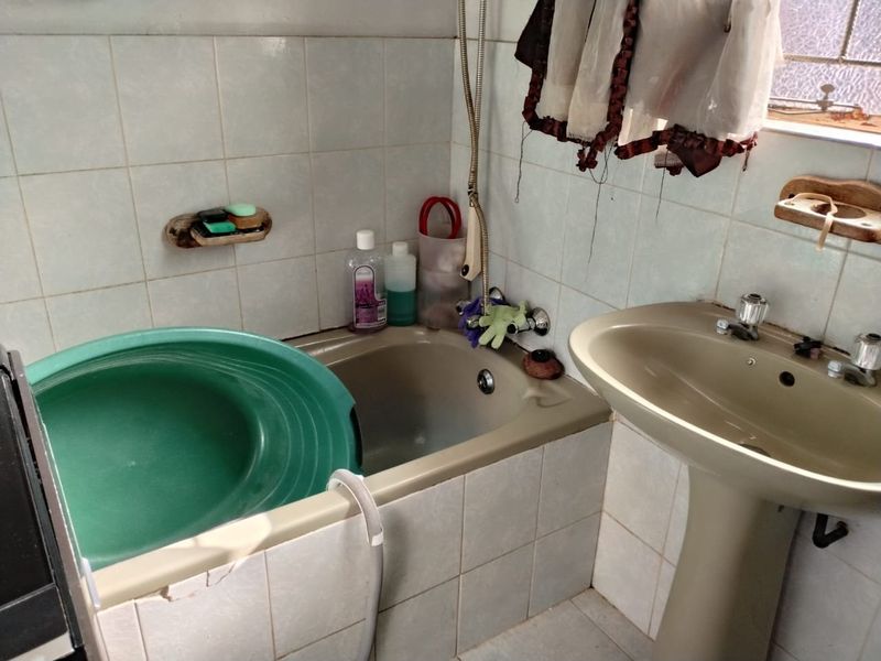 A dated bathroom featuring a pedestal basin and bathtub with tiled walls, requiring cosmetic updates to modernize the space.
