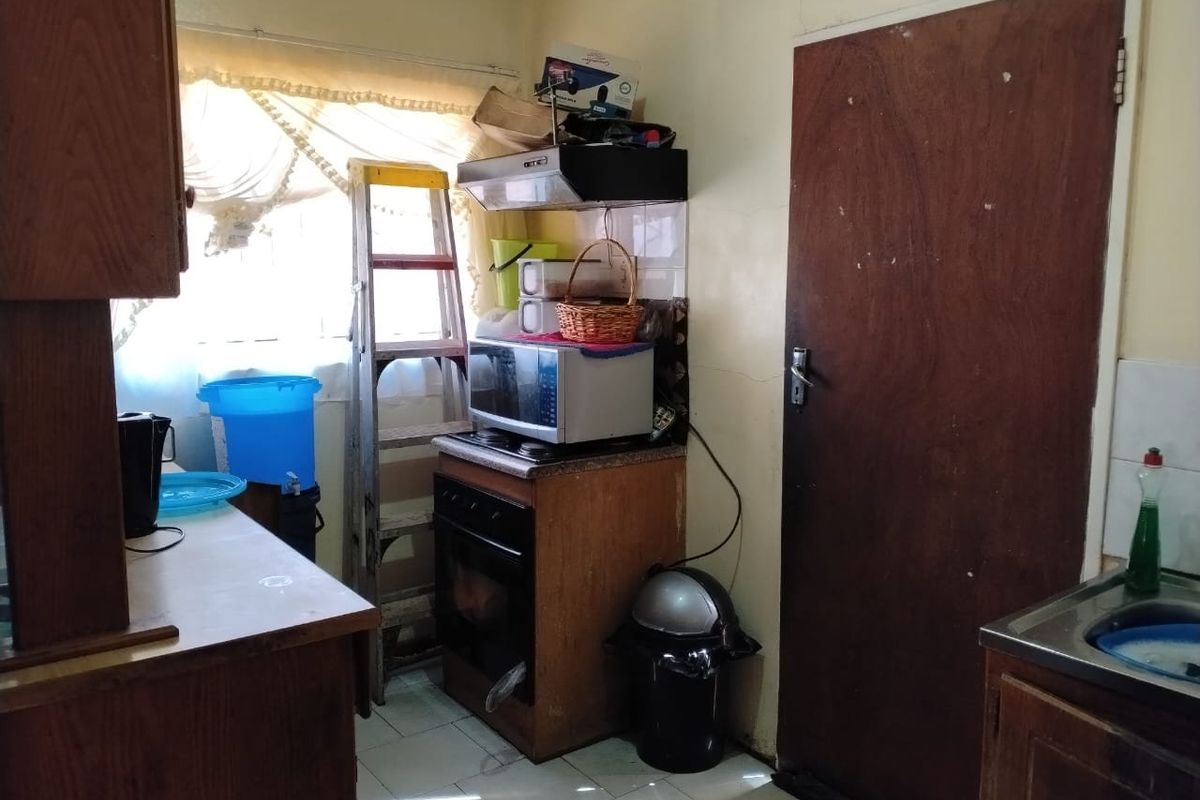 A dated kitchen featuring wooden cabinetry, a built-in oven with extractor fan, and tiled flooring, offering significant potential for modernization and renovation.