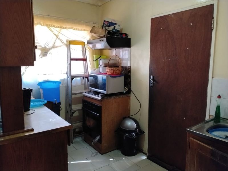 A dated kitchen featuring wooden cabinetry, a built-in oven with extractor fan, and tiled flooring, offering significant potential for modernization and renovation.