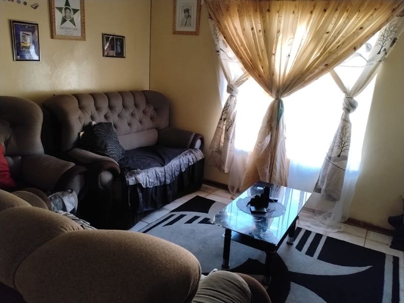 A cozy living room featuring tiled flooring and natural light from a large window with decorative curtains.