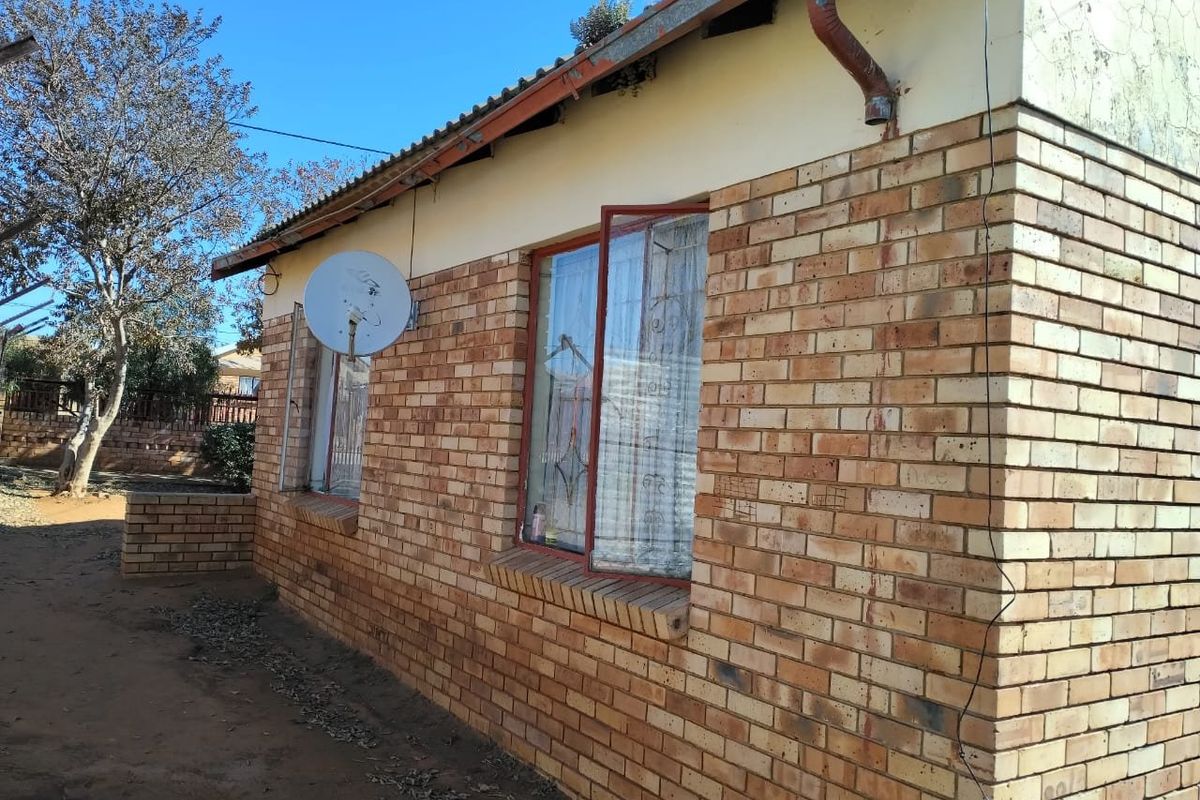 Side view of a face brick house featuring a tiled roof, metal window frames, and an exterior downpipe.