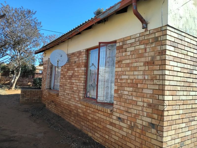 Side view of a face brick house featuring a tiled roof, metal window frames, and an exterior downpipe.