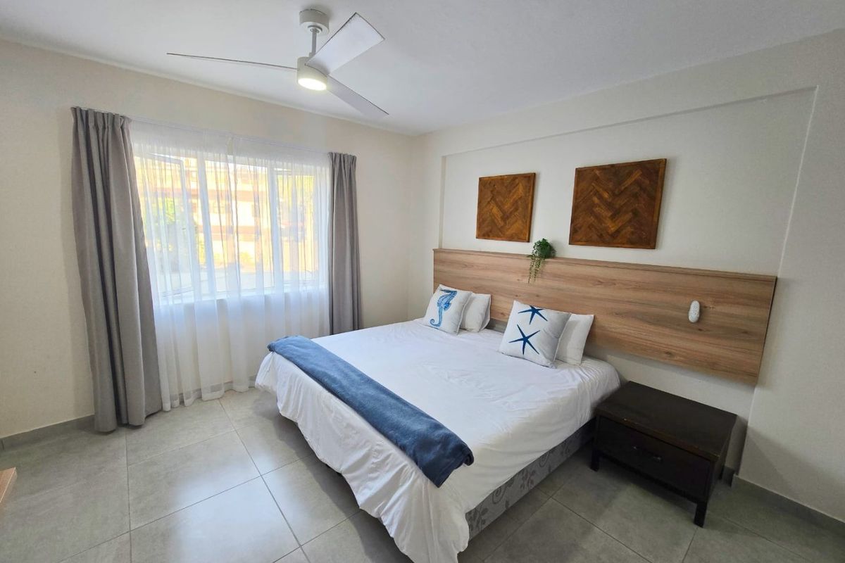 A well-maintained bedroom featuring neutral tiled flooring, a modern ceiling fan, and a built-in wooden headboard.
