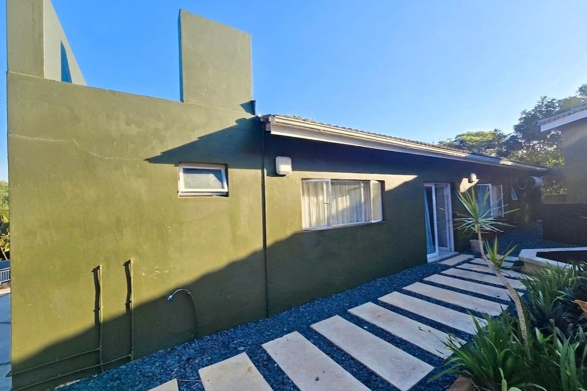 Rear exterior view of the house featuring a painted facade, concrete paver pathway, and sliding door access to the garden area.