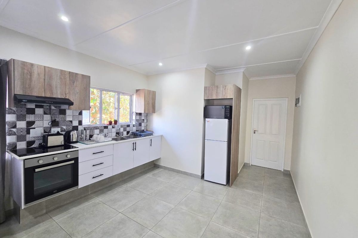 Modern kitchen featuring sleek white and wood-grain cabinetry, tiled backsplash, built-in oven with hob, and neutral floor tiles.