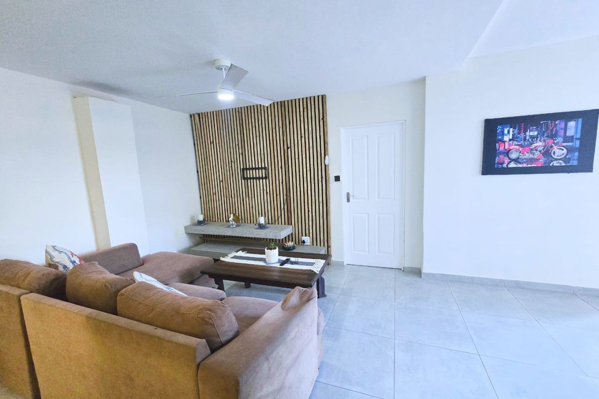 A bright living room featuring a modern timber slat feature wall, built-in concrete shelving, a ceiling fan, and neutral tiled flooring.