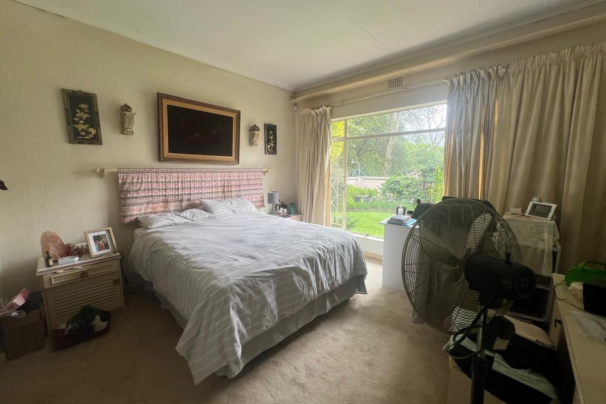 Spacious bedroom featuring large windows with garden views and carpeted flooring, offering a comfortable and well-lit living space.
