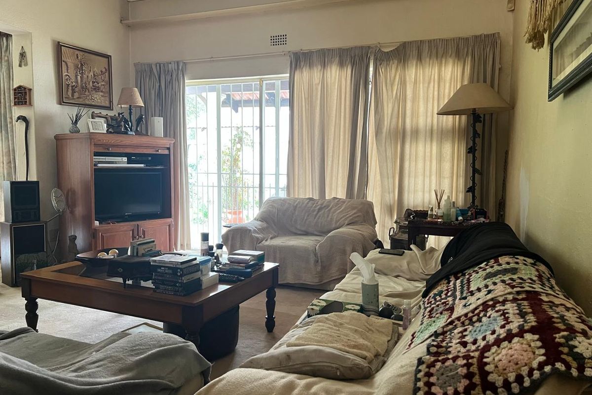 A living room featuring a vaulted ceiling, carpeted flooring, and a sliding glass door with security gate leading to the exterior.