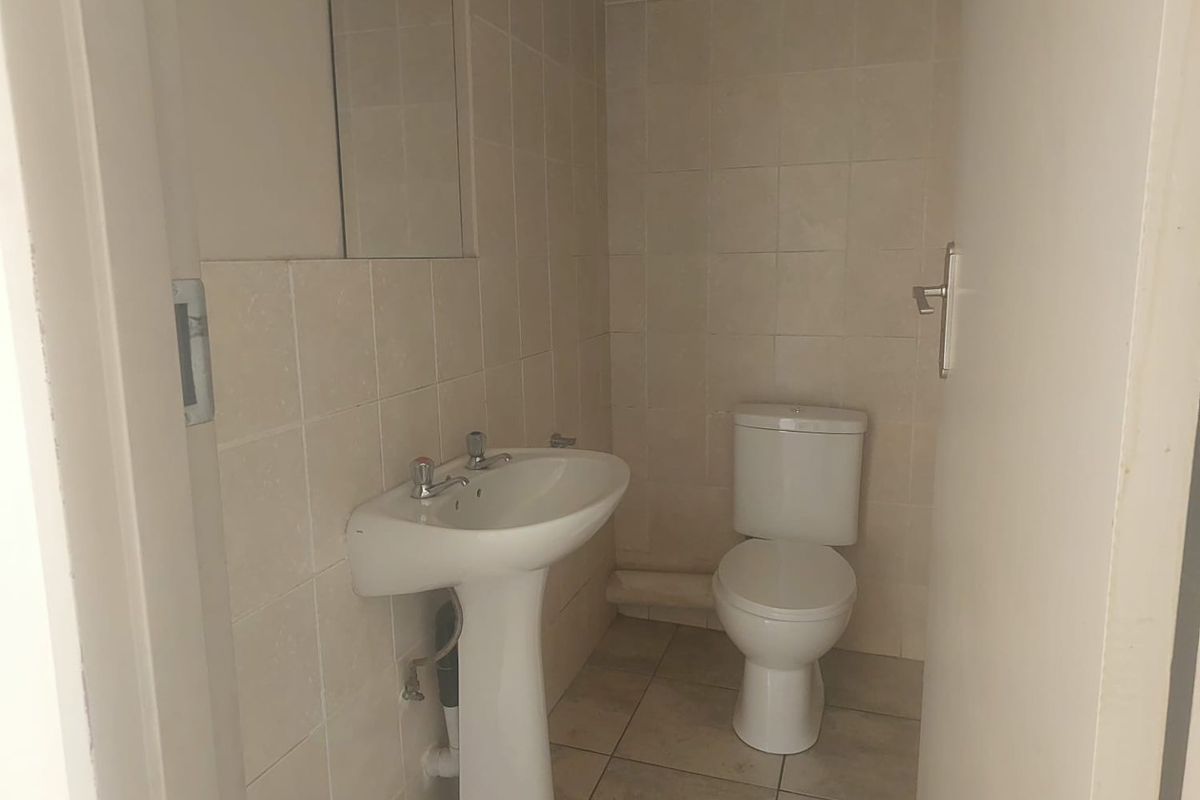 A functional guest bathroom featuring a pedestal basin, ceramic toilet, and neutral wall and floor tiling.