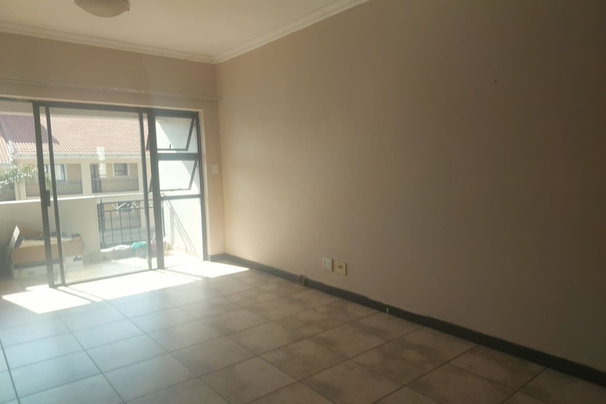 An empty, tiled living room featuring a large sliding glass door that provides access to an outdoor balcony area.