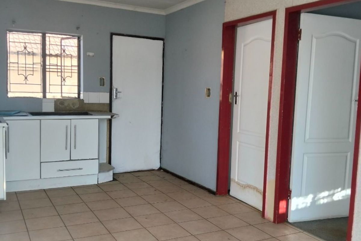 An empty kitchen area featuring tiled flooring, basic cabinetry, and direct access to adjacent rooms through multiple doorways.