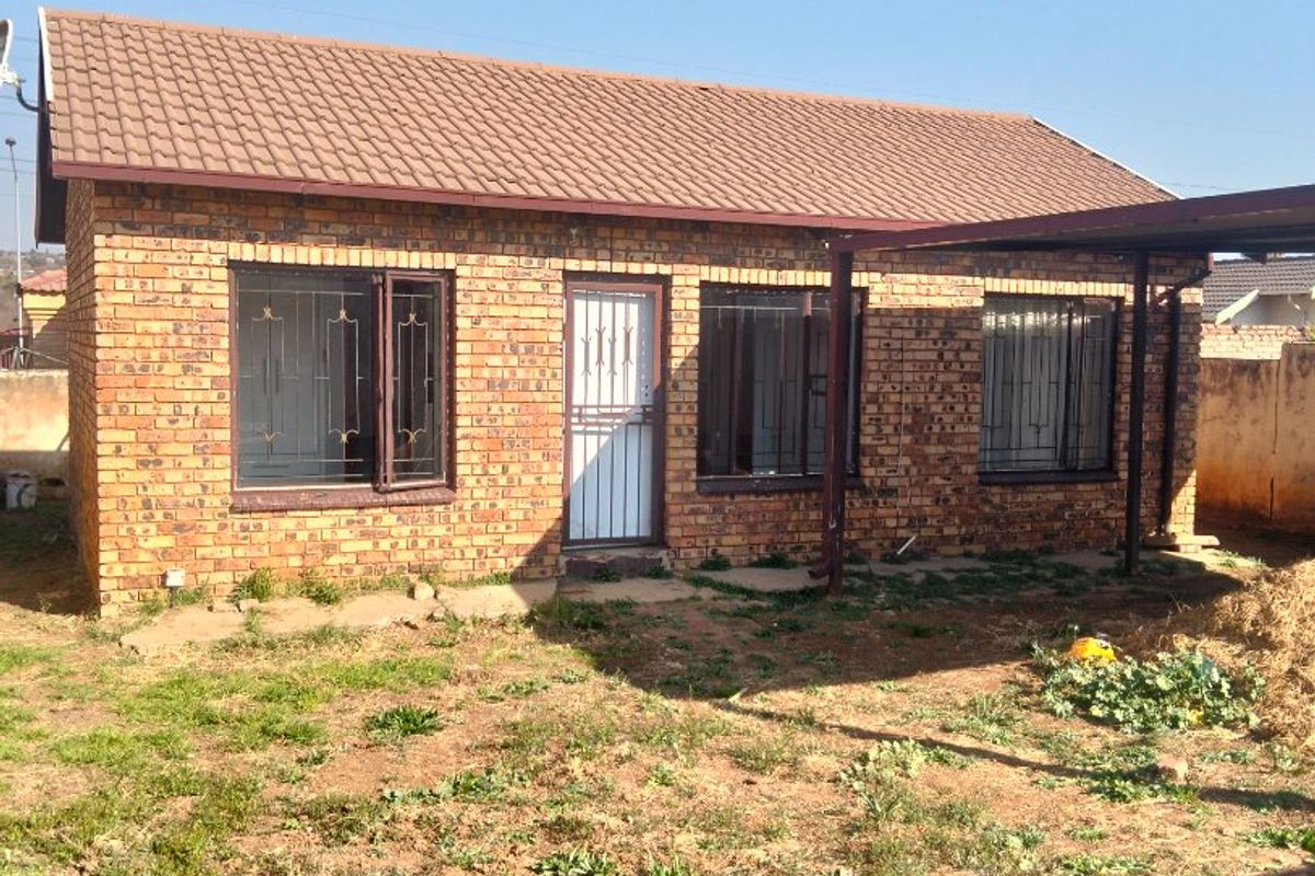 A single-story face brick house featuring a tiled roof, security bars on windows, and a covered patio area overlooking the rear yard.