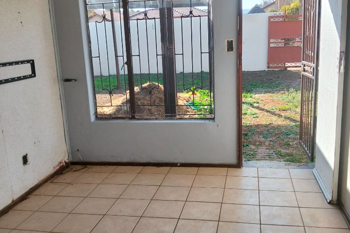An empty living room featuring tiled flooring, security bars on the window, and direct access to the rear garden through a security gate.