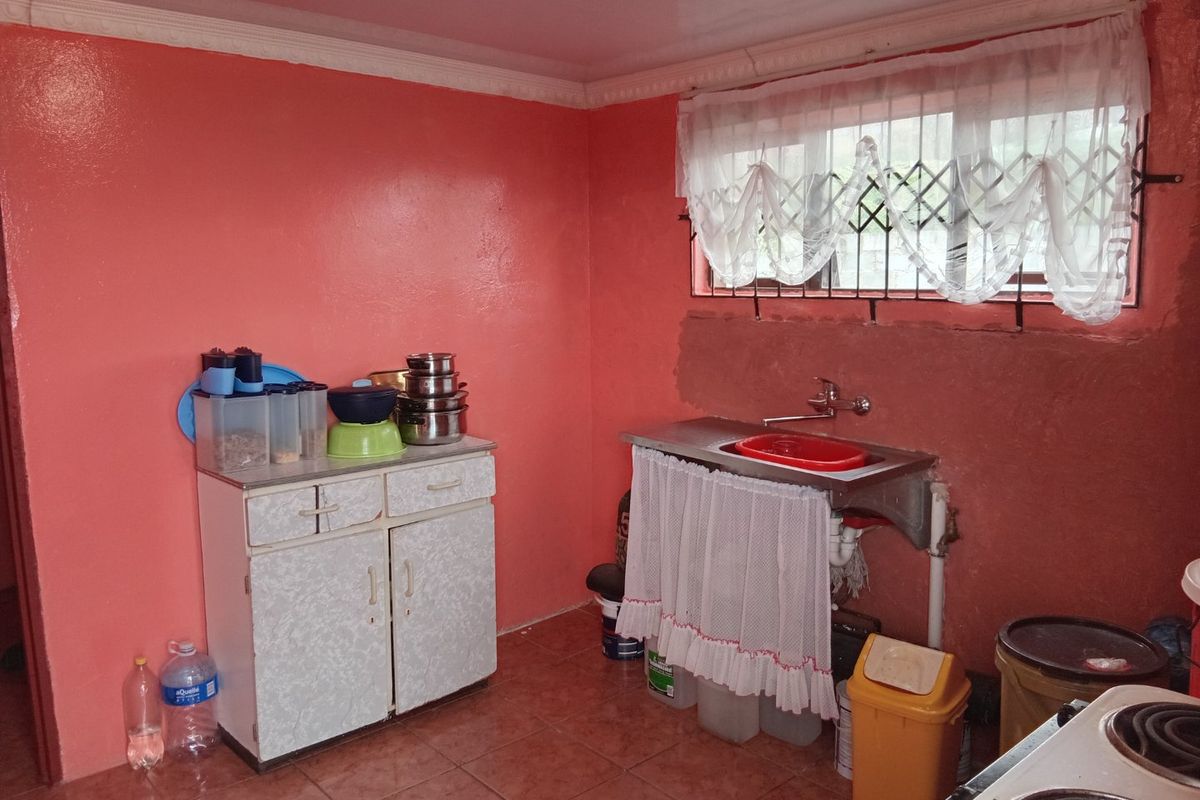 A functional kitchen area featuring tiled flooring, a stainless steel sink, and built-in cabinetry, requiring cosmetic updates to the wall finishes.