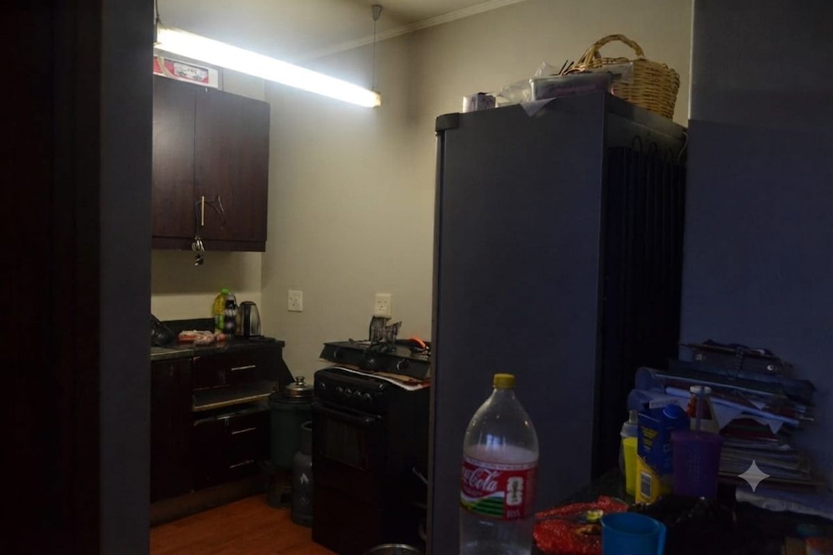 A compact kitchen area featuring dark wood cabinetry, a freestanding oven, and laminate flooring, requiring updated lighting and finishes to improve functionality and aesthetic appeal.