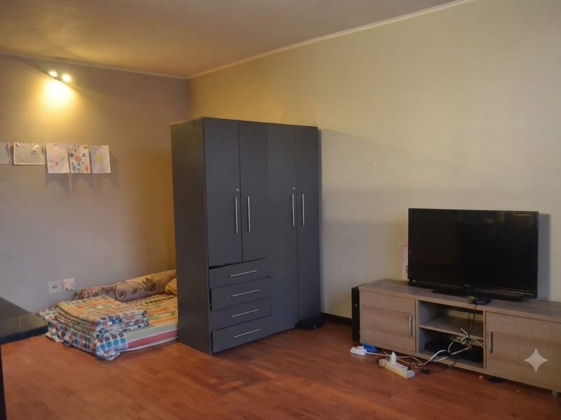 A bedroom featuring laminate flooring and recessed lighting, currently utilized with a wardrobe and television unit.